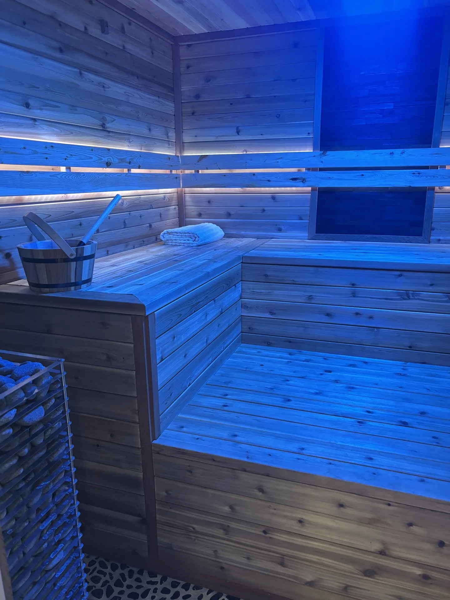 Sauna room interior with blue chromotherapy lighting, cedar bench, and HUUM heater